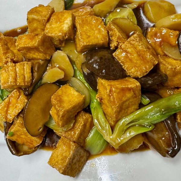 Close-up of golden fried tofu, green vegetables, and mushrooms in a rich brown sauce.