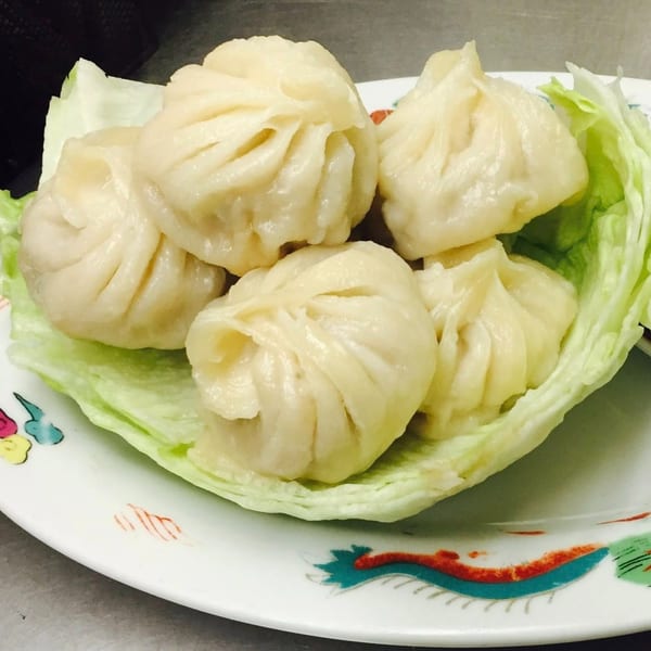 Five steamed dumplings, or momos, nestled on a bed of fresh lettuce on a decorative plate.