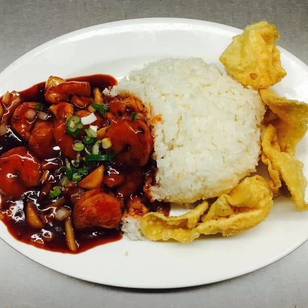 Sweet and sour chicken with rice and fried wontons on a white plate.